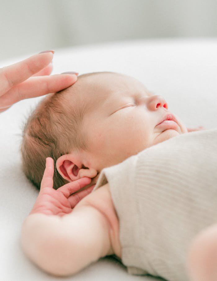 Close-up of a serene newborn baby sleeping, gently touched by hand in soft natural light.